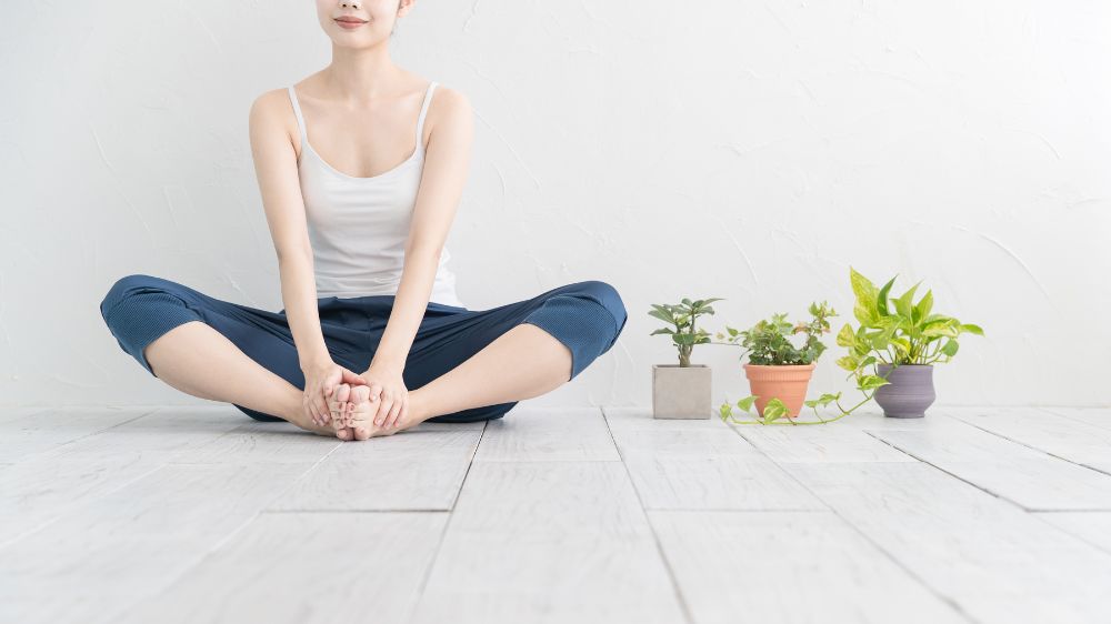 屋内であぐらをかいてストレッチの準備をしている女性