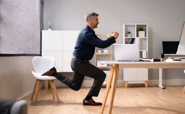 オフィスで椅子に片足を乗せてブルガリアンスクワットをする男性