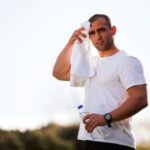 運動をして水分補給しつつ汗を拭く男性