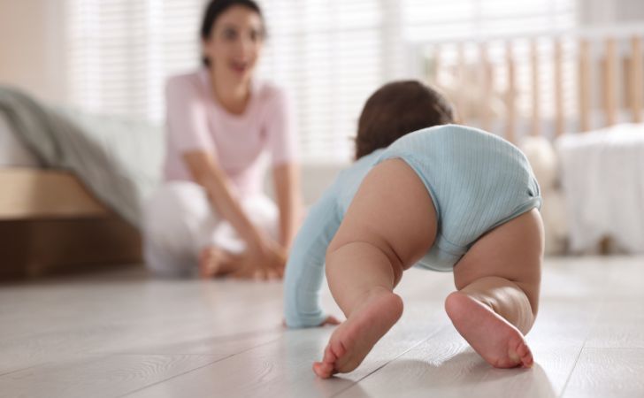 ハイハイをする赤ちゃんと笑顔で見守る母親